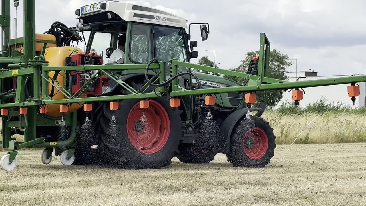 Ein am Traktor angebautes Spritzgestänge mit WeSee-Nachrüstung, dessen Einzeldüsenventile in kurzen, gezielten Stößen über ein Feld spritzen.