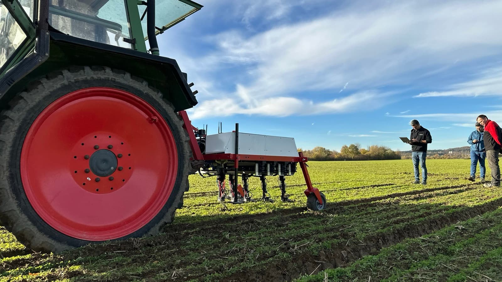 DynamoBot-Team prüft Live-Daten von WeWeed auf einem Tablet neben dem traktorgeführten Roboter auf dem Feld.